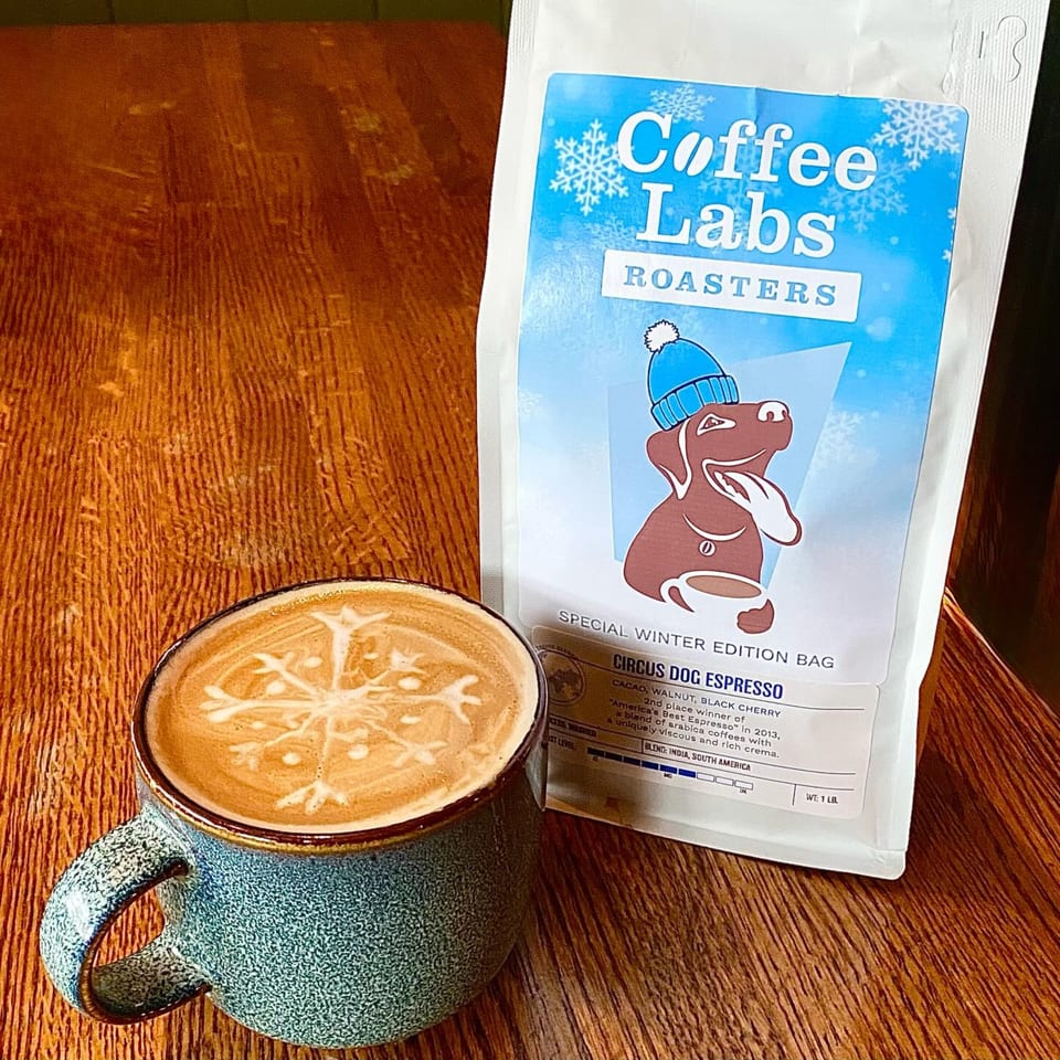 A latte with snowflake art and a bag of Coffee Labs Roasters Circus Dog Espresso on a wooden table.