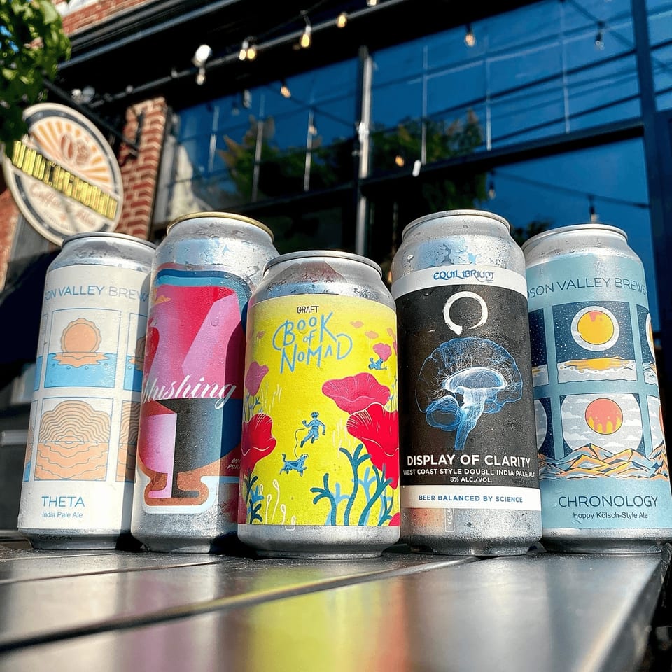 Five colorful craft beer cans, some with condensation, on a table outside Underground Coffee & Ales.