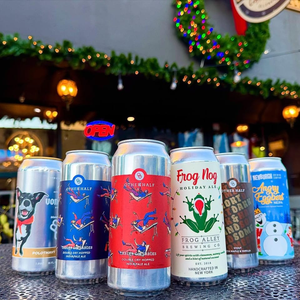Six craft beer cans with festive labels sit on a metal table outside Underground Coffee & Ales.